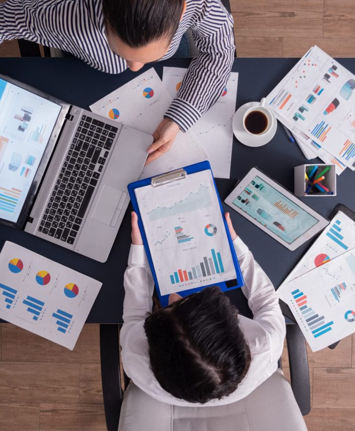 Top viewTop view of manager and employee doing teamwork in business office , looking at charts on laptop display. Finance paperwork with charts at workplace. Discusing financial plan.
